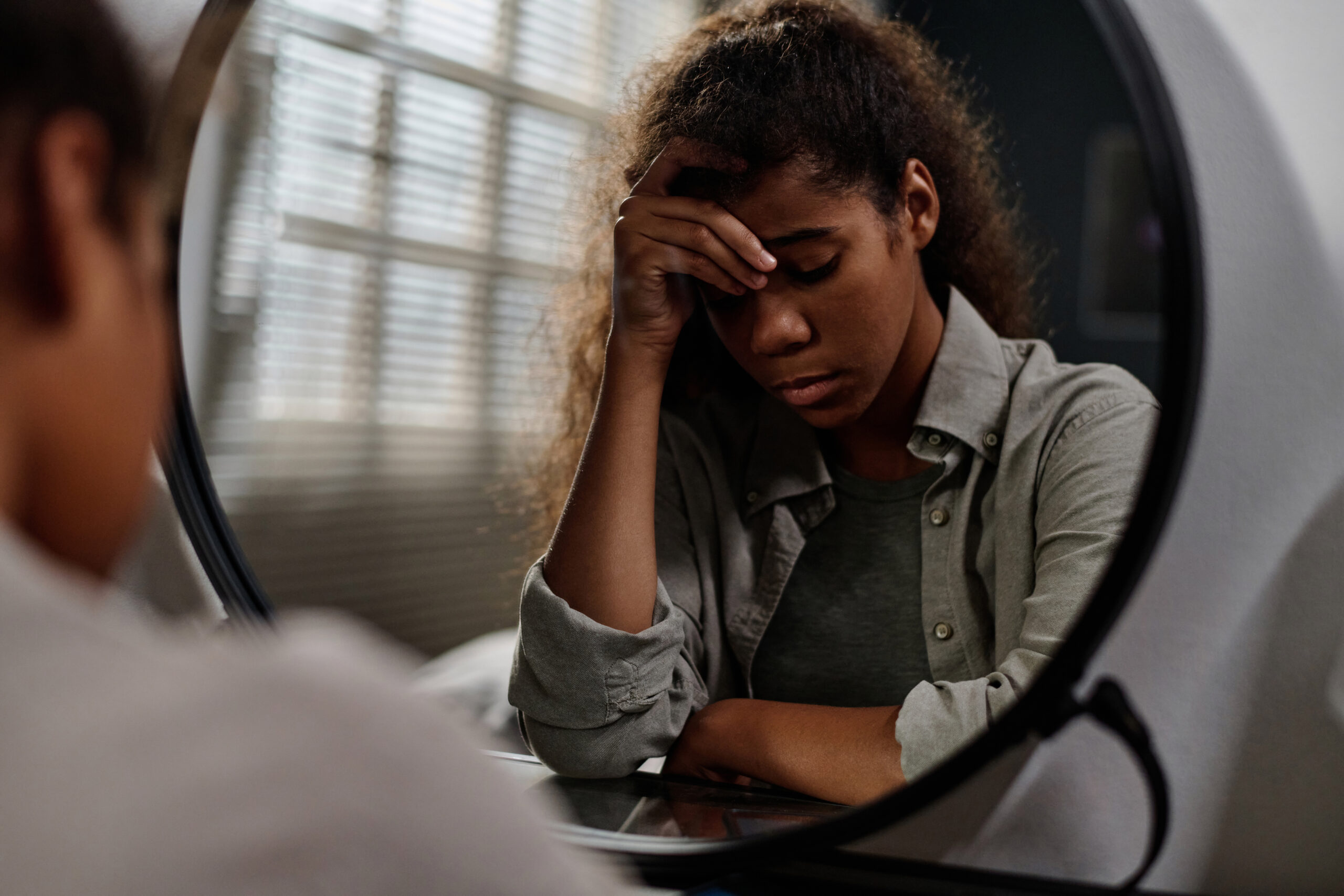 Offended teenage girl touching her forehead while sitting in front of mirror